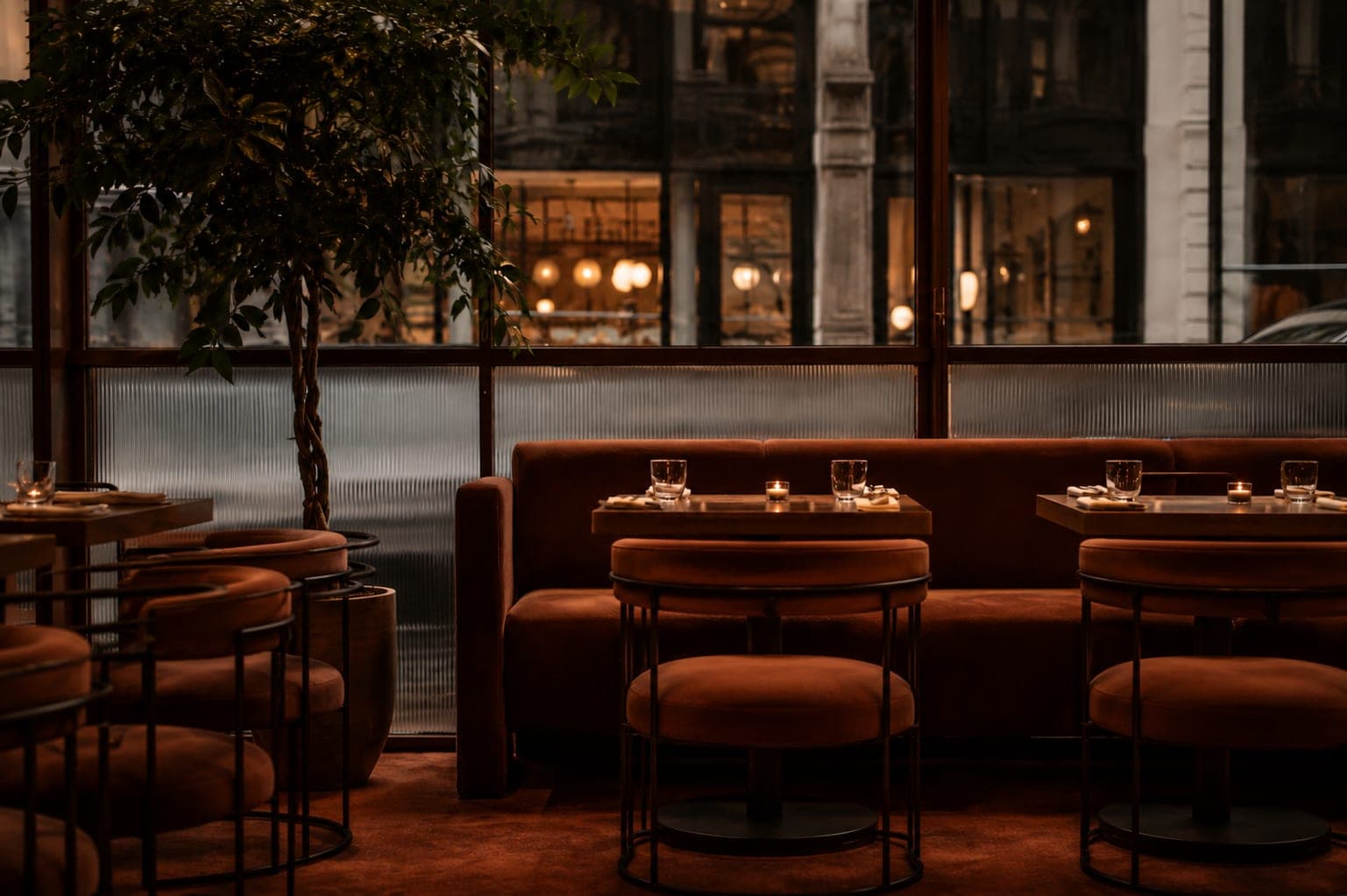 Salle d'un restaurant gastronomique parisien, banquettes velours et tables dressées à la lumière des bougies