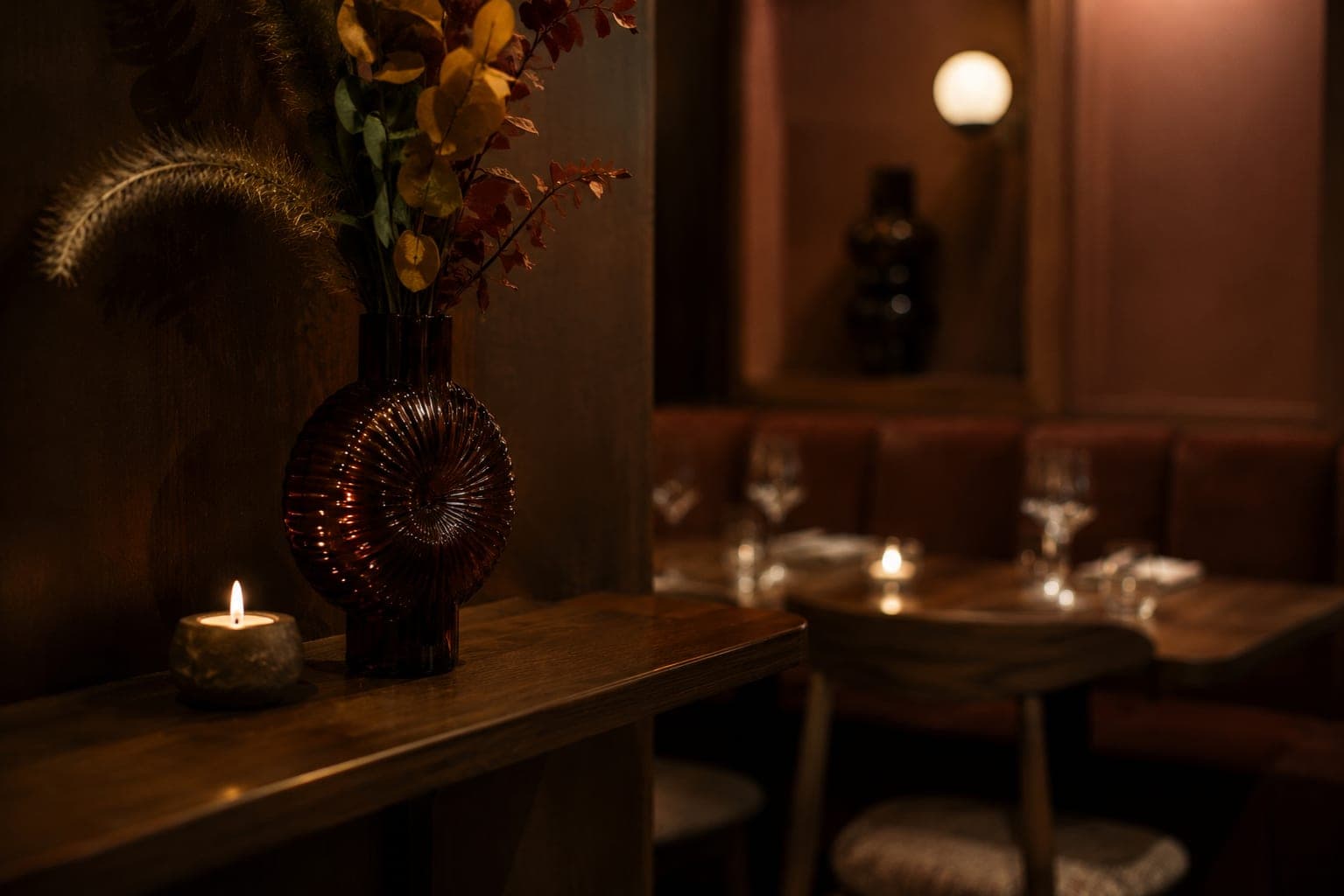 Détail feutré d'un restaurant gastronomique : bougie, vase et tables dressées en arrière-plan